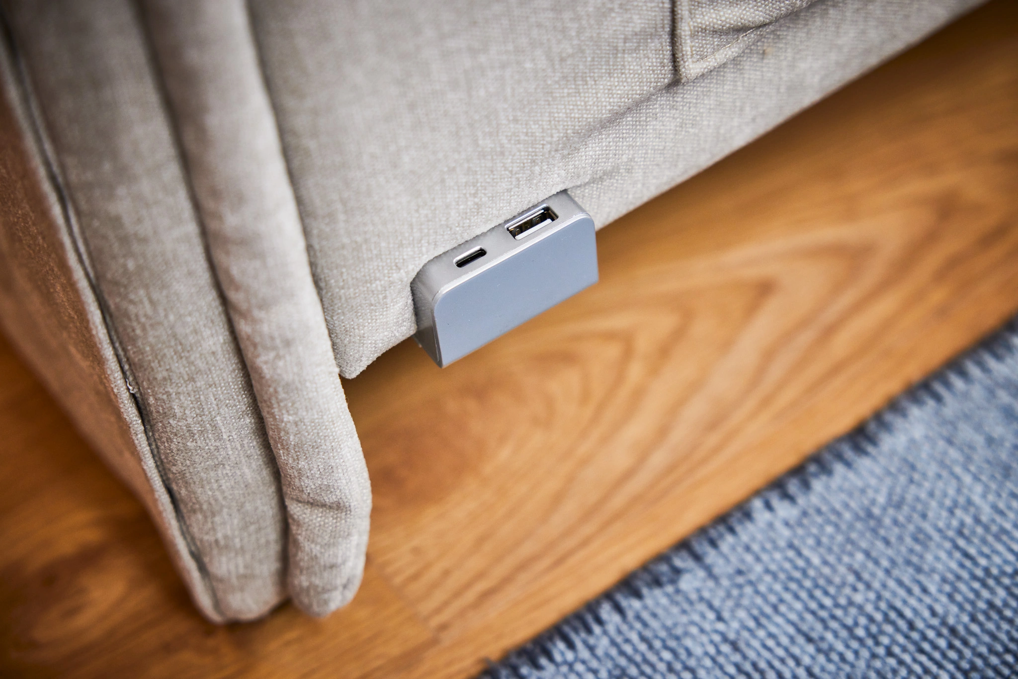 Port USB intégré dans un canapé beige, sur sol en bois avec tapis gris, pratique pour recharger appareils électroniques.