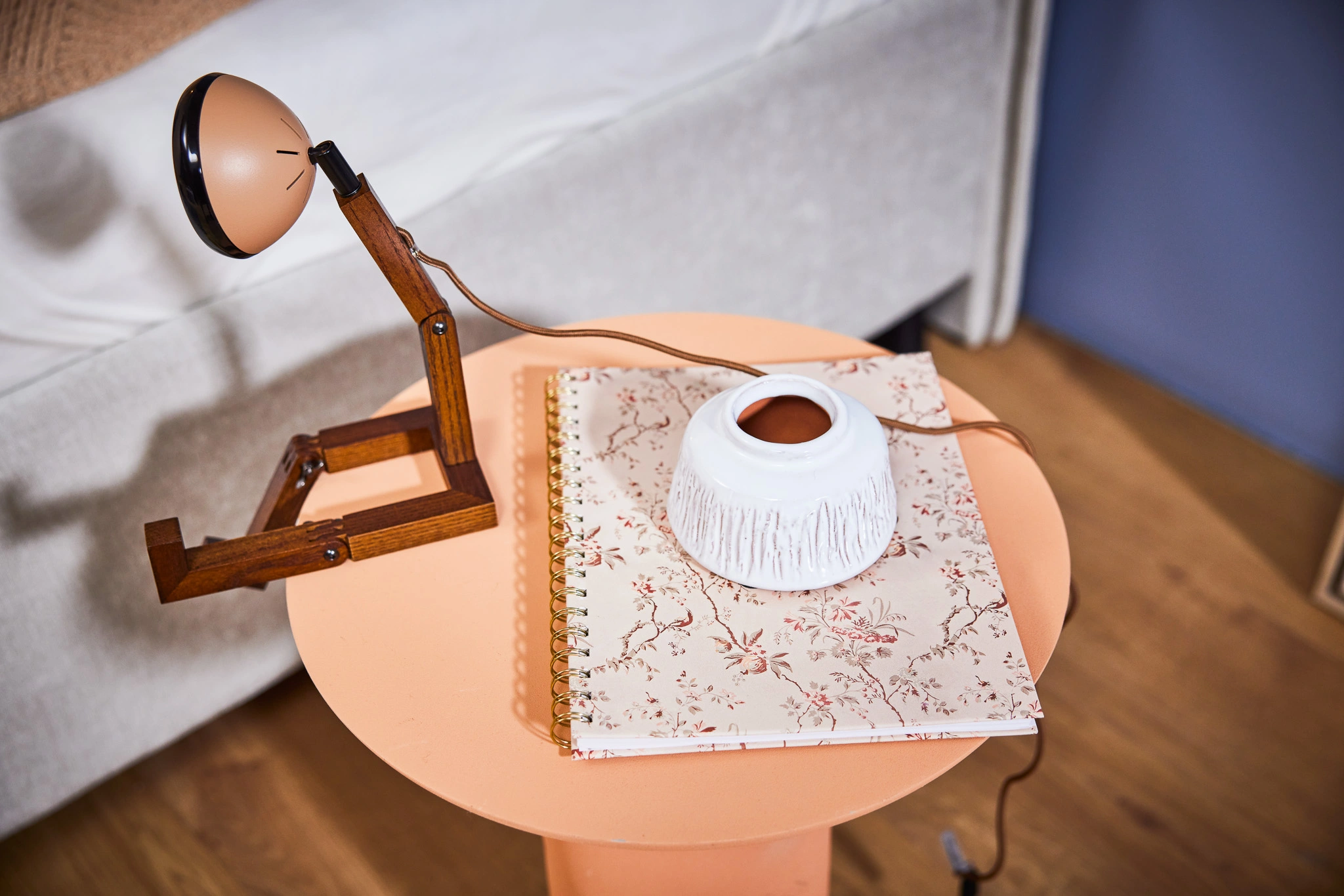 Lampe de bureau vintage en bois sur une table ronde orange, avec carnet à motifs floraux et pot blanc en céramique pour décoration intérieure élégante.