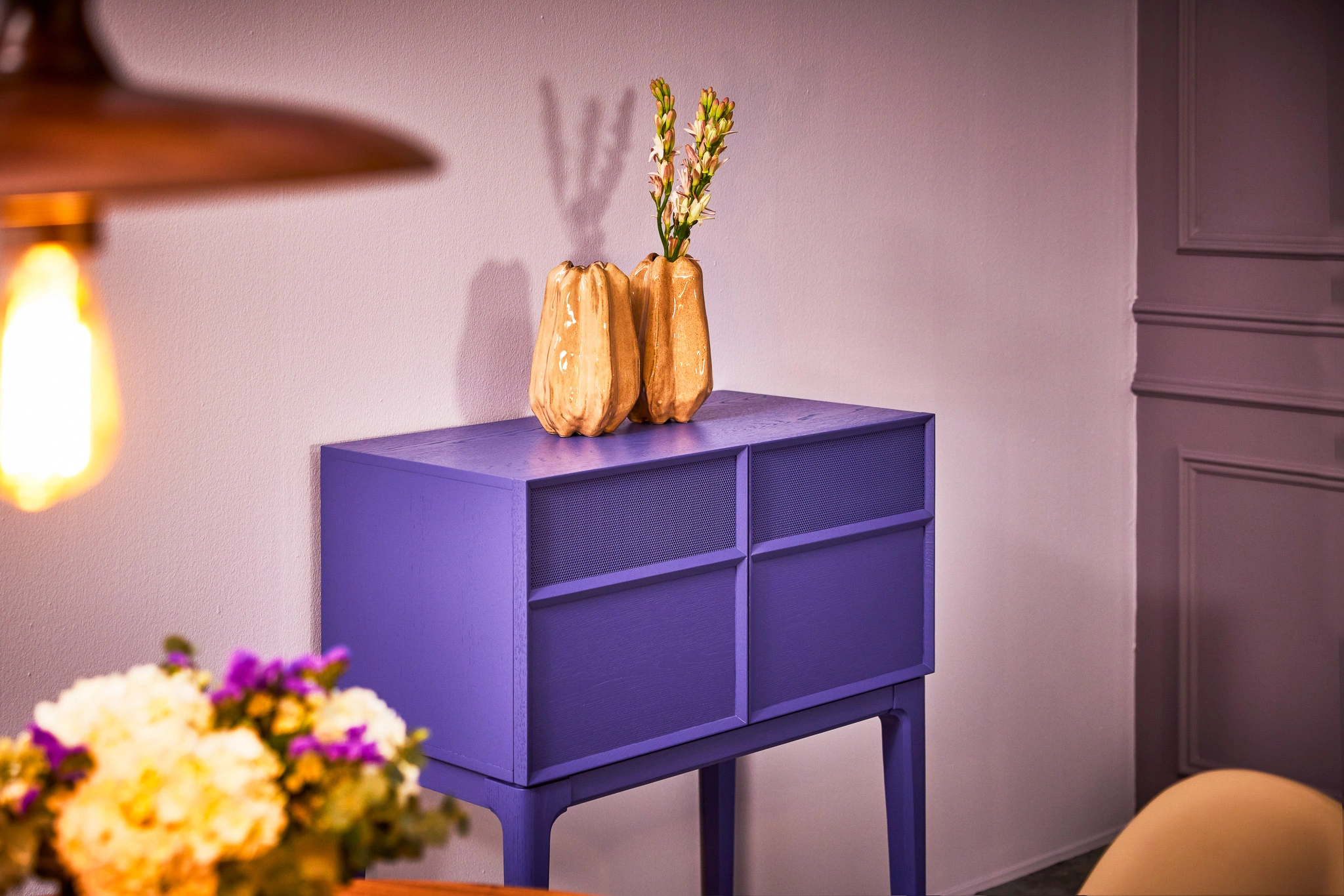 Commode violette avec décorations en céramique beige et fleurs blanches, éclairage chaleureux. Décoration intérieure moderne et élégante.