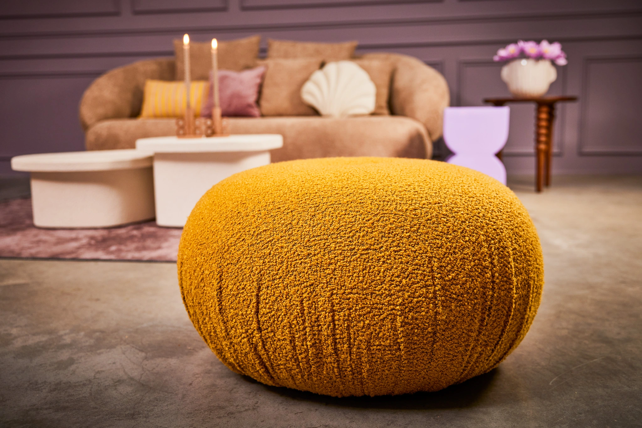 Pouf jaune en tissu texturé dans un salon moderne avec canapés et tables design, créant une ambiance chaleureuse et élégante.