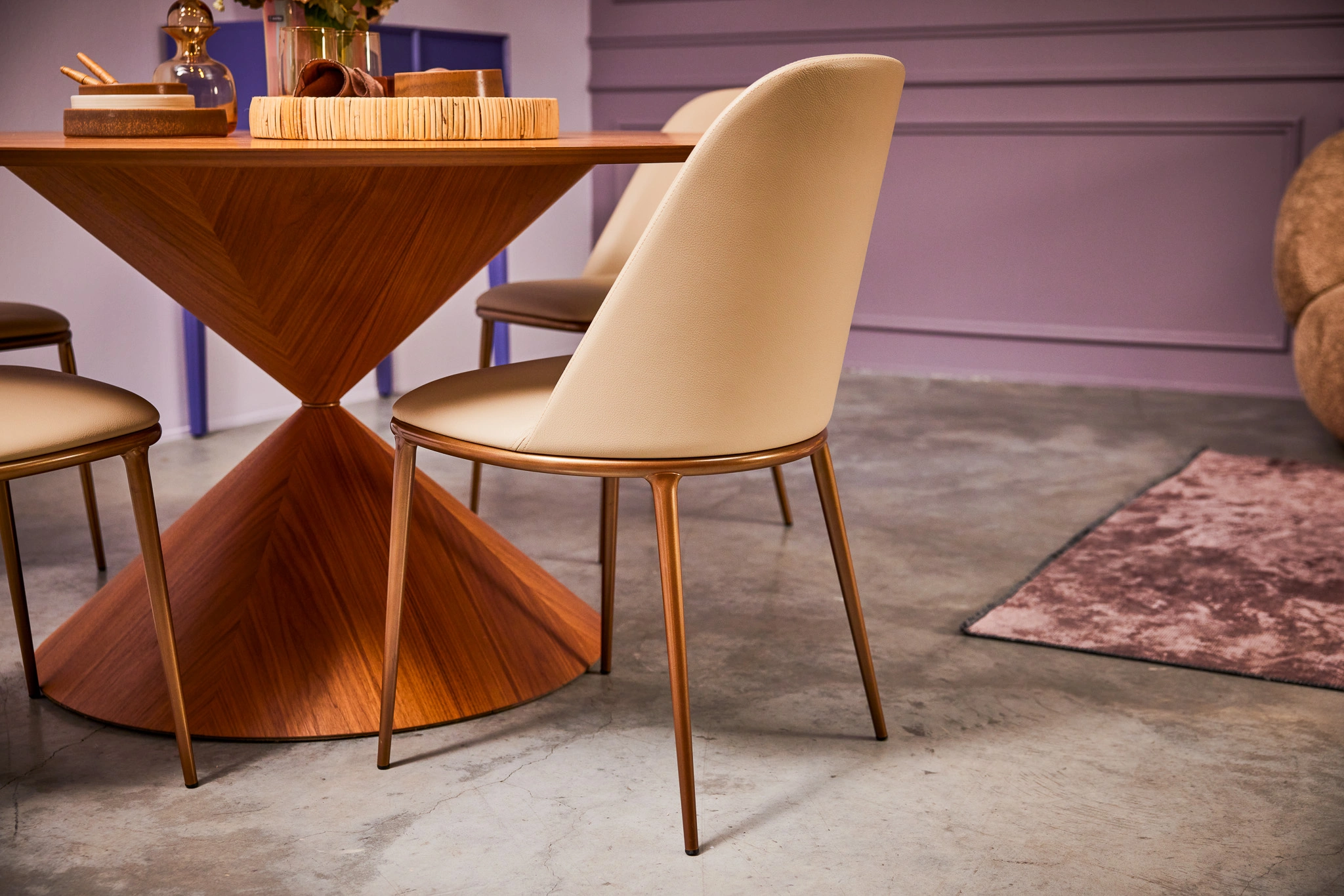 Salle à manger moderne avec table en bois au design unique, chaises beige élégantes et sol en béton. Ambiance chic et contemporaine.