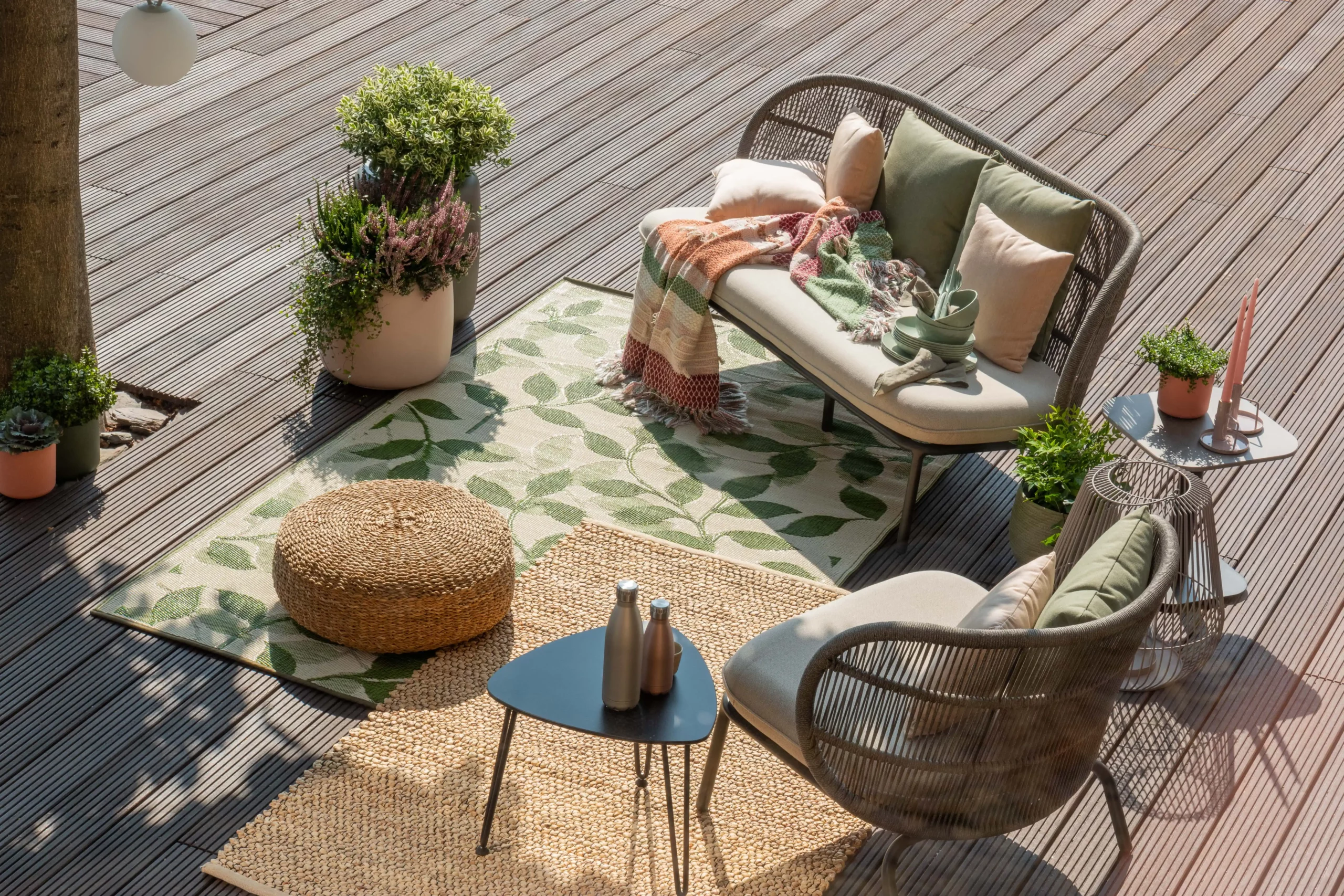 Aménagement terrasse : coin détente avec mobilier en rotin, tapis à motifs feuillages et accessoires naturels pour une ambiance conviviale et zen.