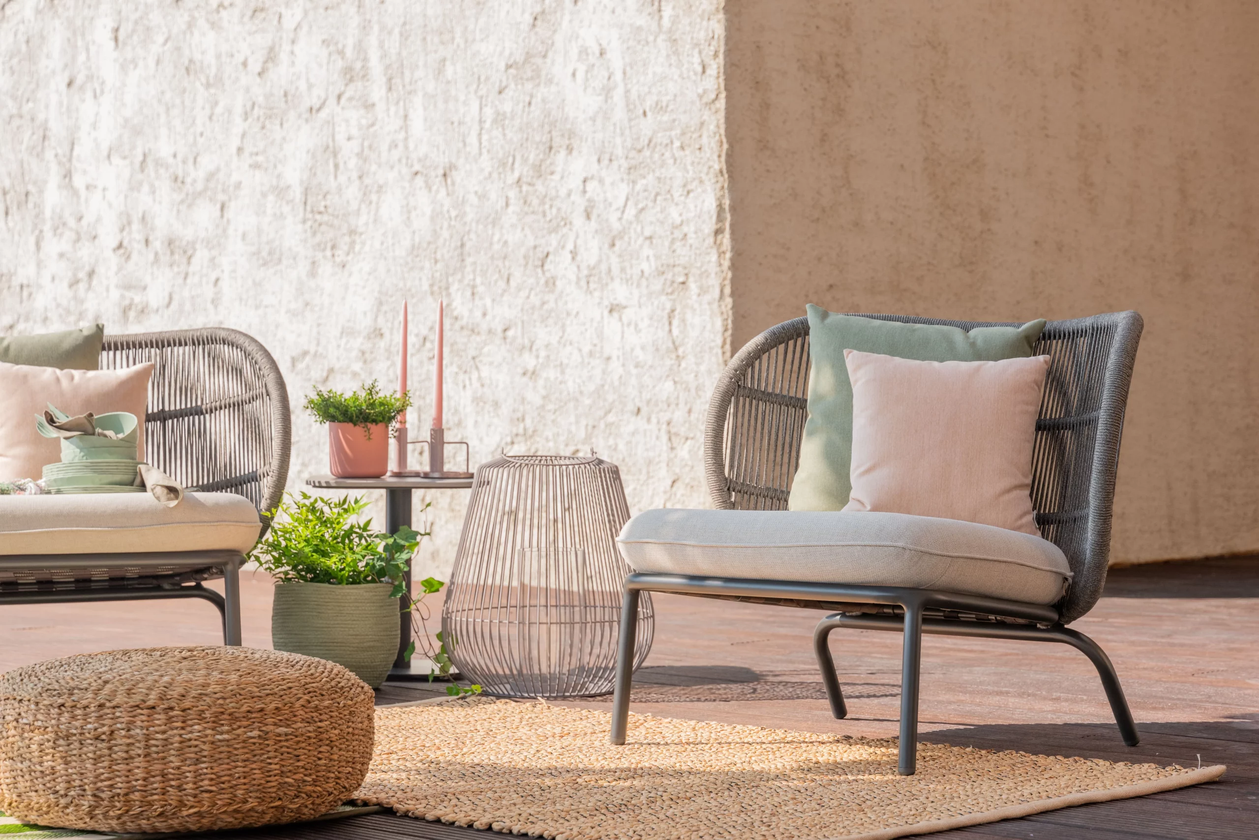 Mobilier de terrasse moderne : fauteuil en rotin avec coussins pastel, pouf tressé et déco végétale pour une ambiance naturelle et conviviale en extérieur.