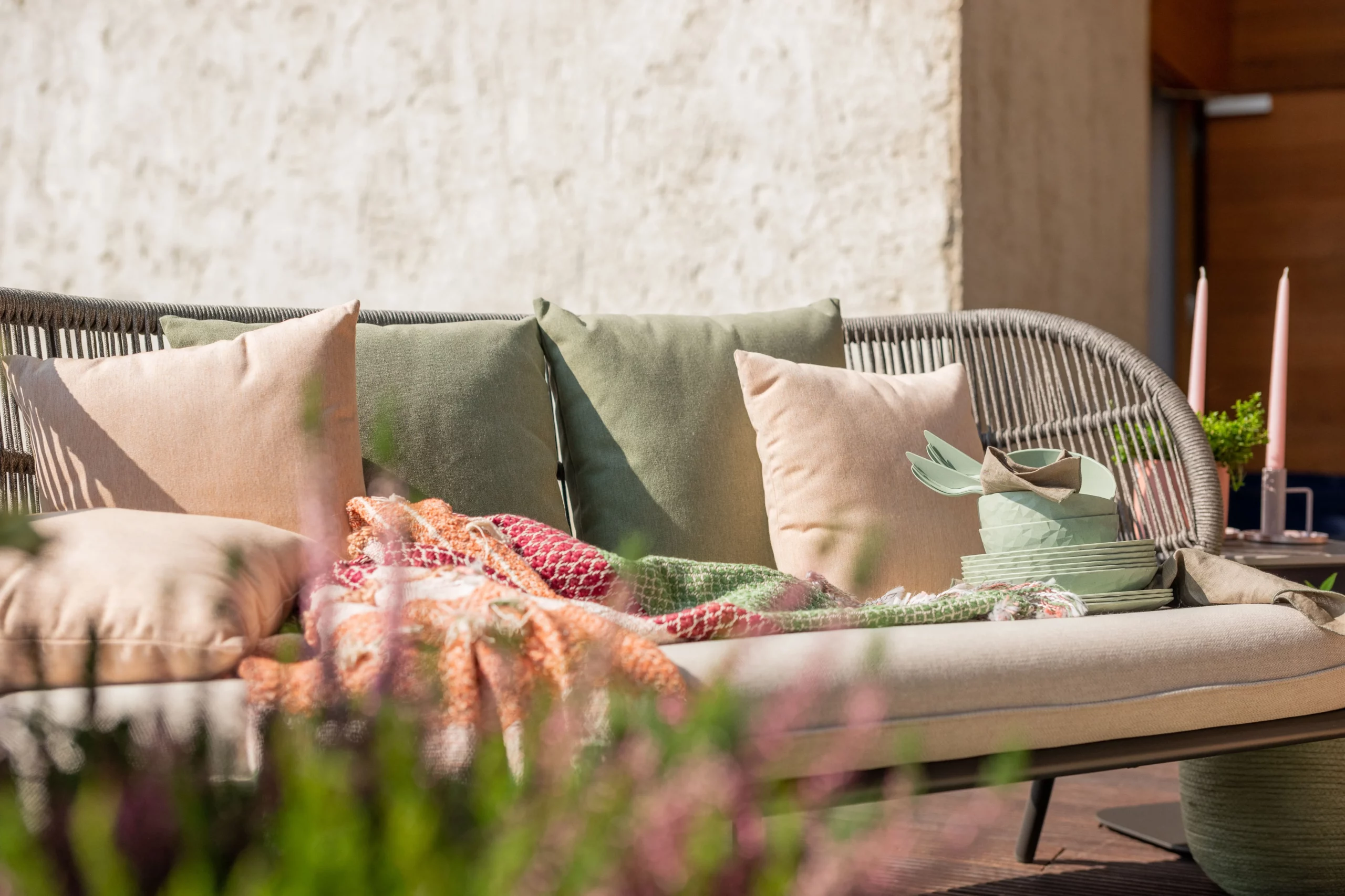 Canapé de terrasse en rotin avec coussins pastel et plaid cosy, idéal pour créer un espace extérieur chaleureux et élégant pour vos moments de détente.