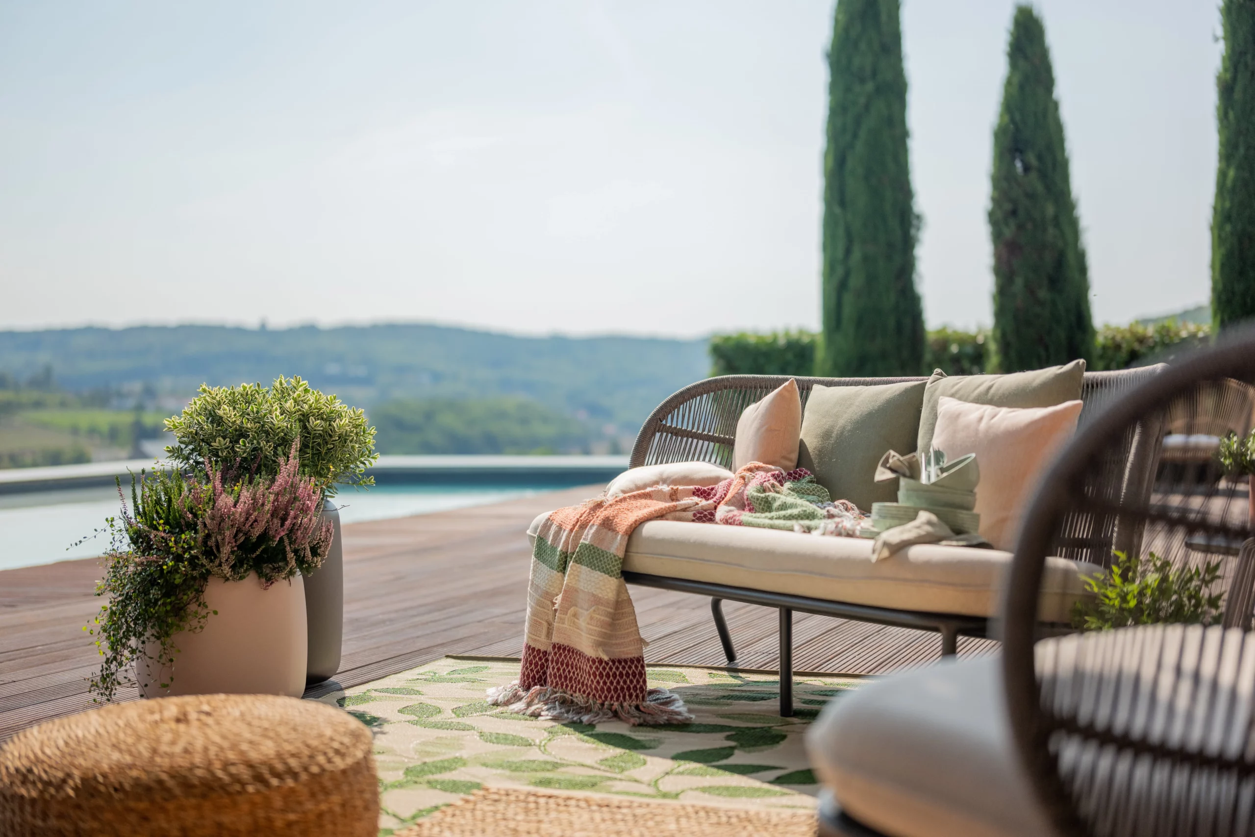 Terrasse avec vue panoramique : canapé en rotin, tapis à motifs végétaux et déco naturelle, pour un espace extérieur élégant et relaxant au bord de la piscine.